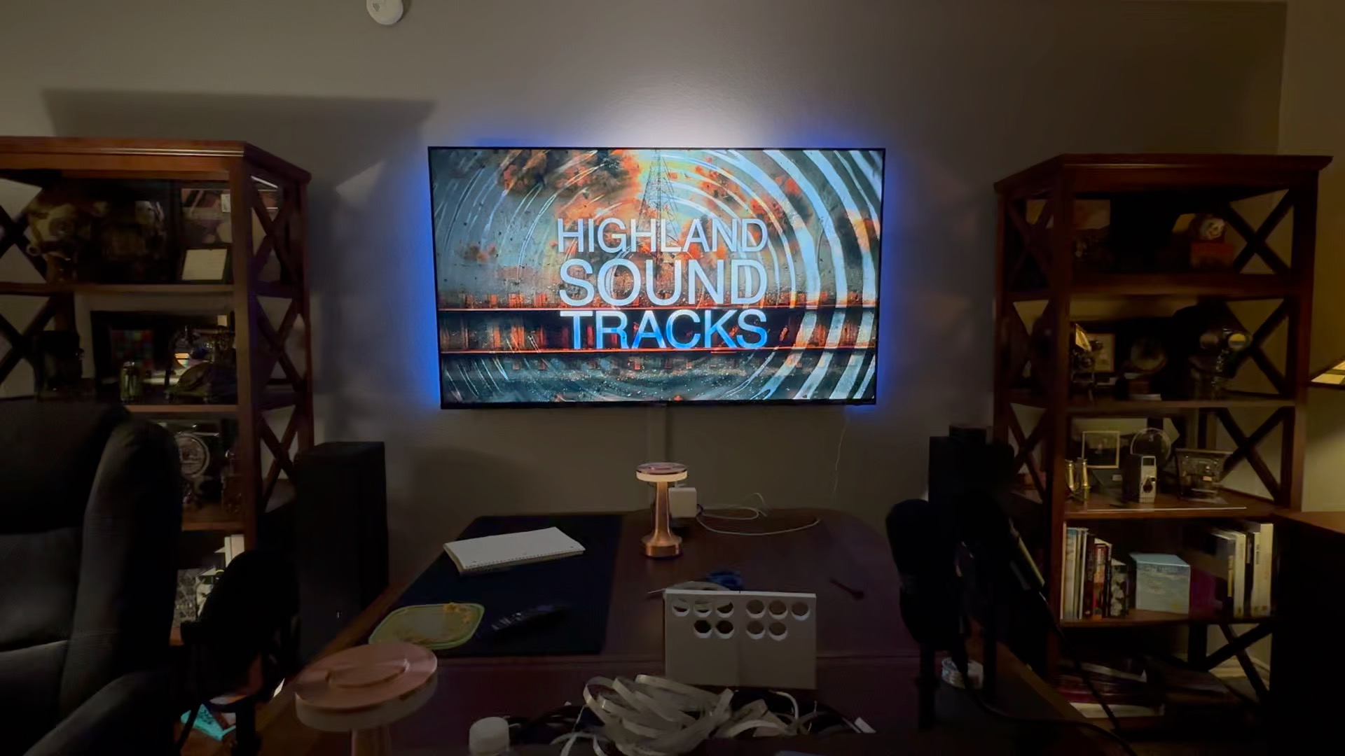 Finished podcast set: HST logo on wall-mounted TV with blue LED backlighting, shelves flanking