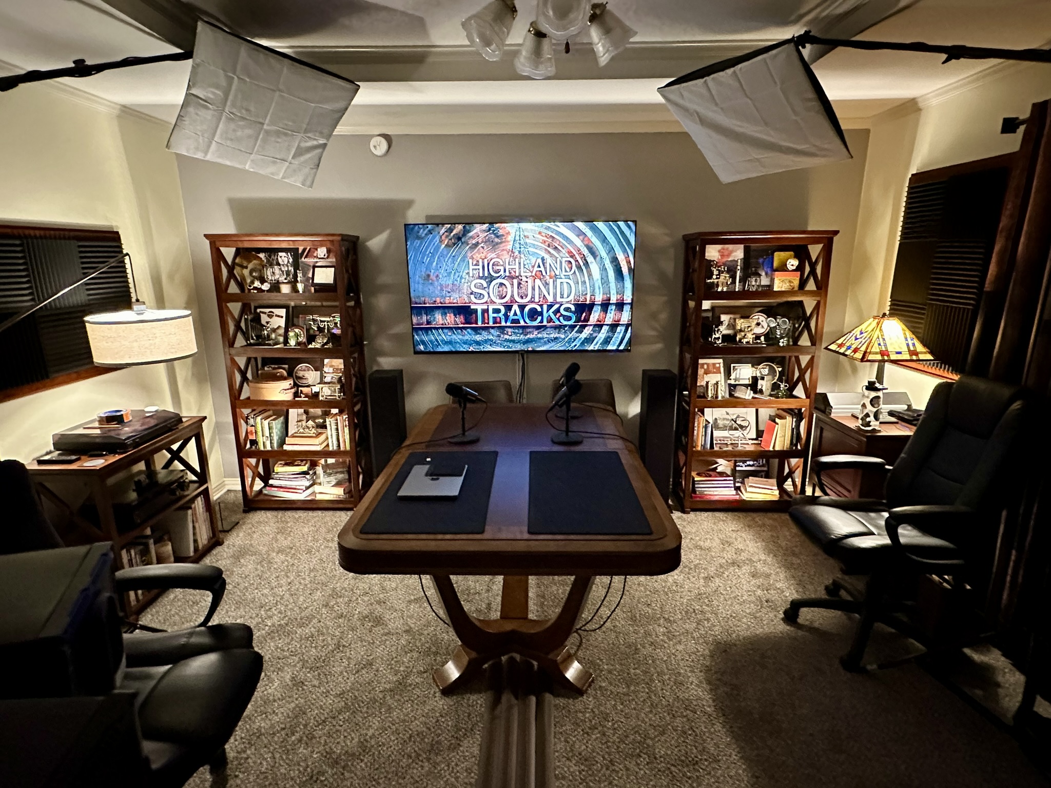 Completed podcast studio: HST logo on mounted TV, shelving, mics, softbox lighting