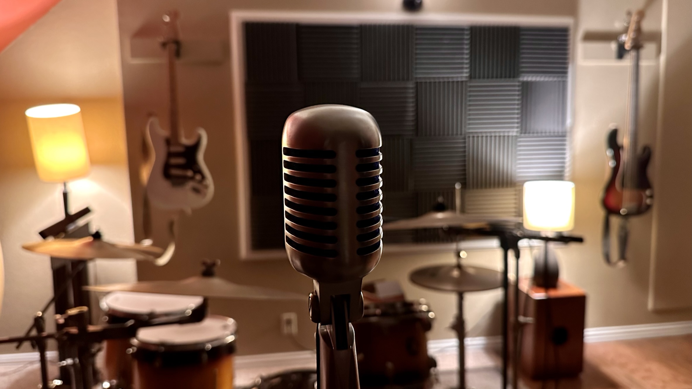 Vintage mic center frame, drum kit and acoustic panels behind, guitars on wall