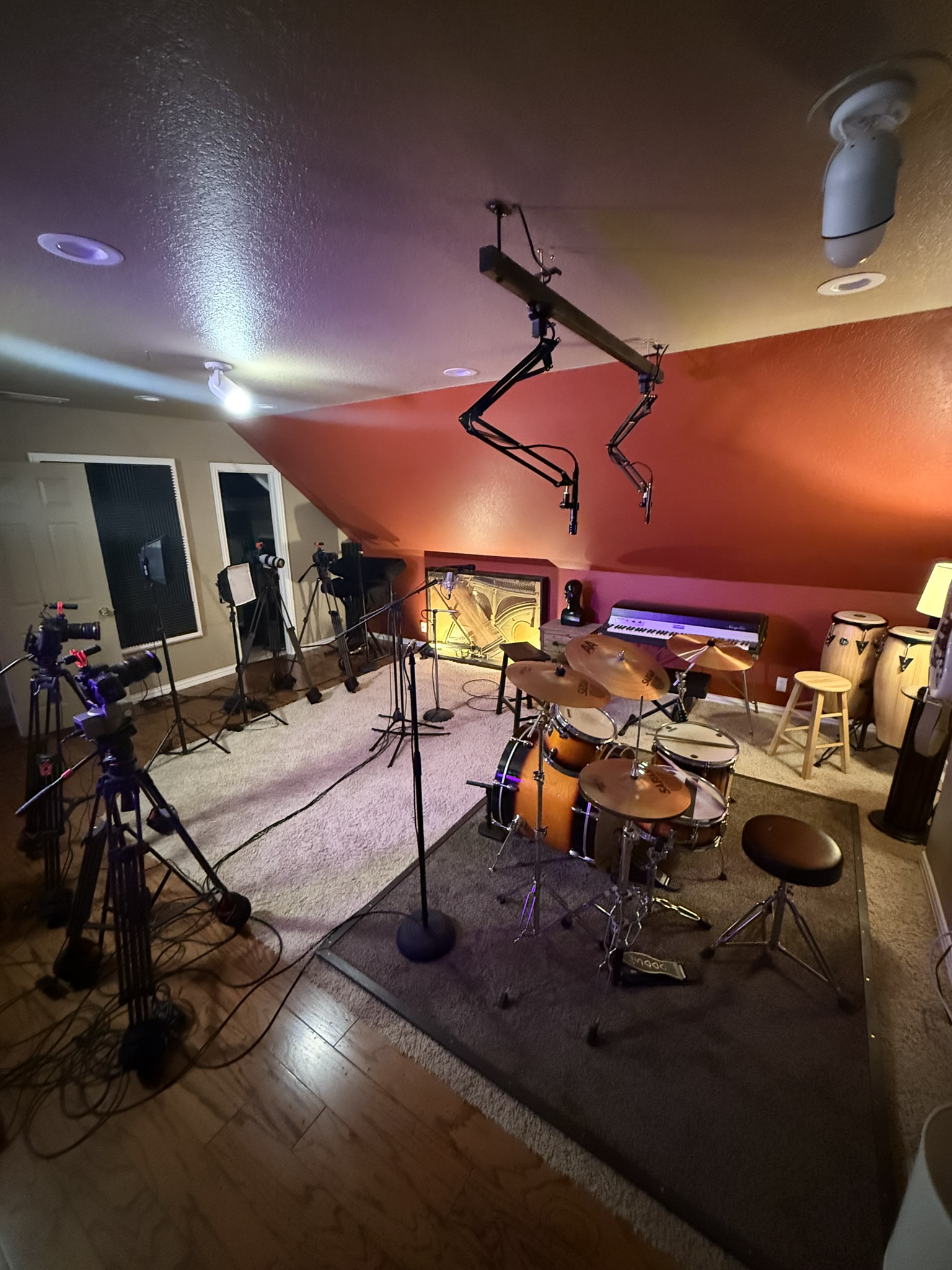 Performance studio: drum kit, overhead boom mics, cameras, keyboards, congas, purple lighting